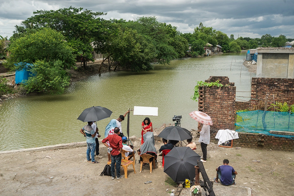 A field producer facilitating an intimate interview with a local woman in a rural Bangladeshi village.