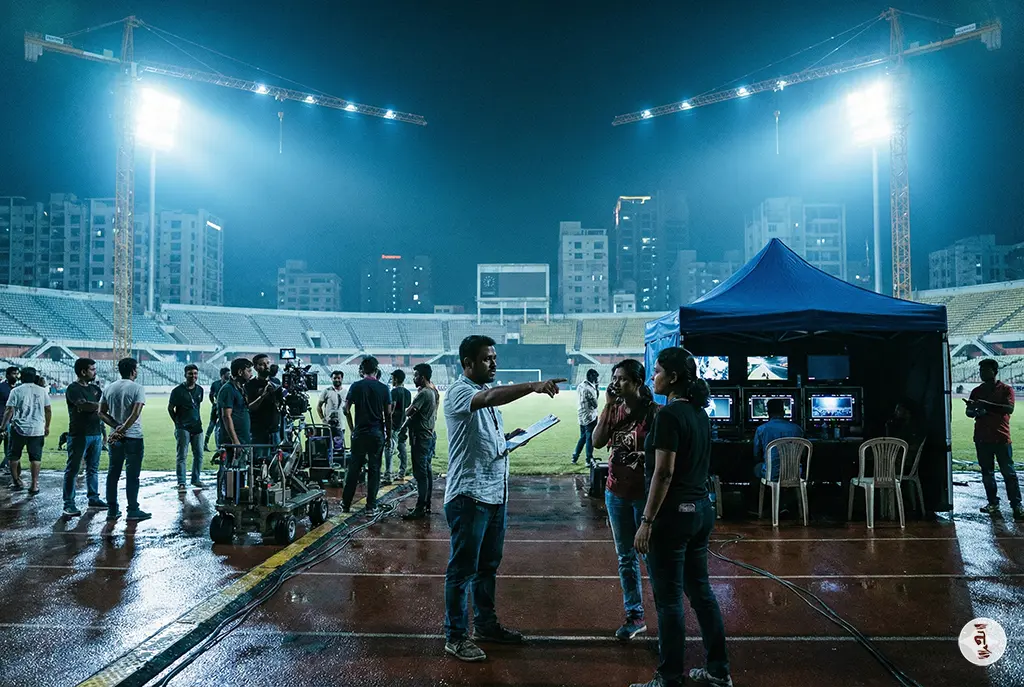 A large scale commercial film set in Dhaka with heavy lighting equipment, monitors, and a large local crew.